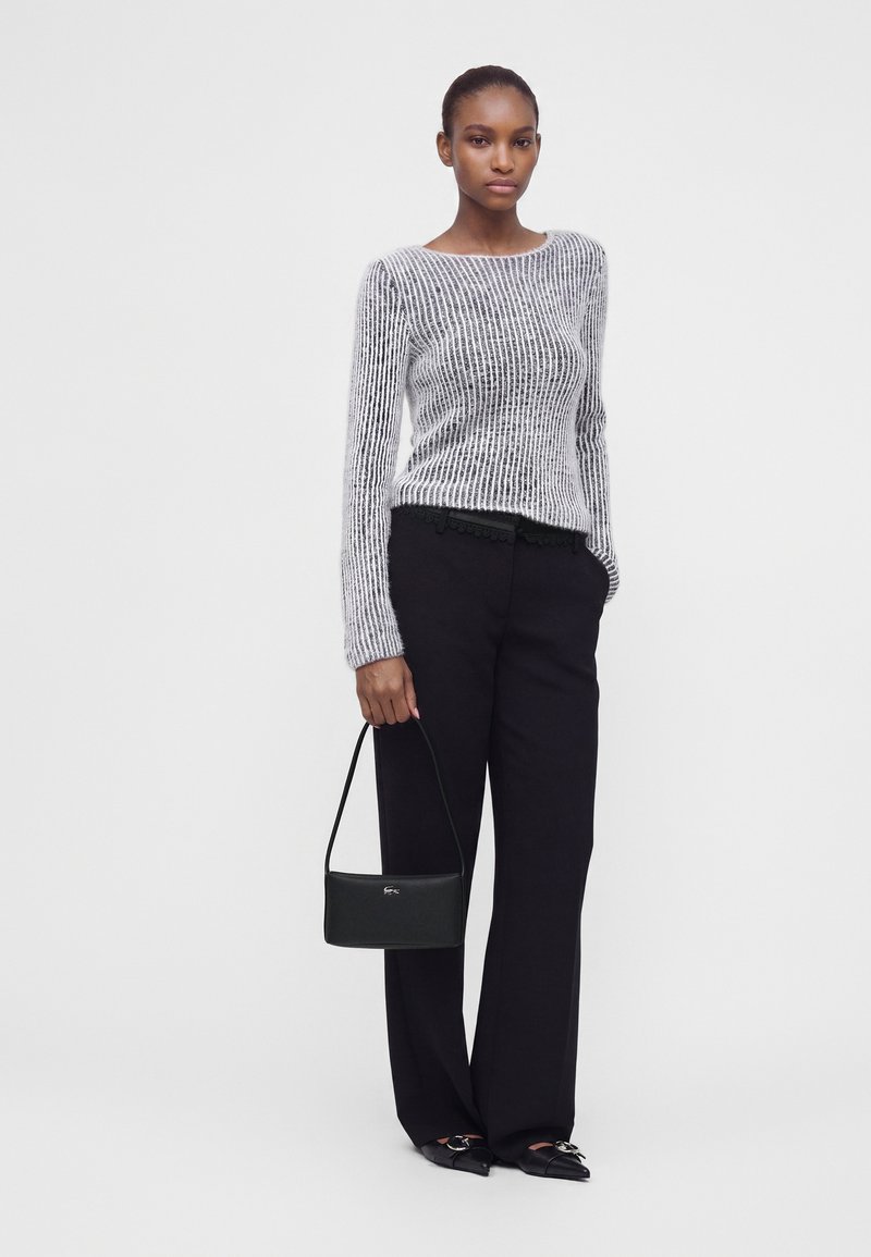 Femme portant un pull gris rayé à manches longues, un pantalon noir à jambes larges, des ballerines noires pointues, et tenant un petit sac à main noir.