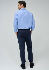 Camisa de manga larga azul claro con puños enrollados, combinada con pantalones de cintura elástica en azul marino oscuro y botas negras hasta el tobillo.