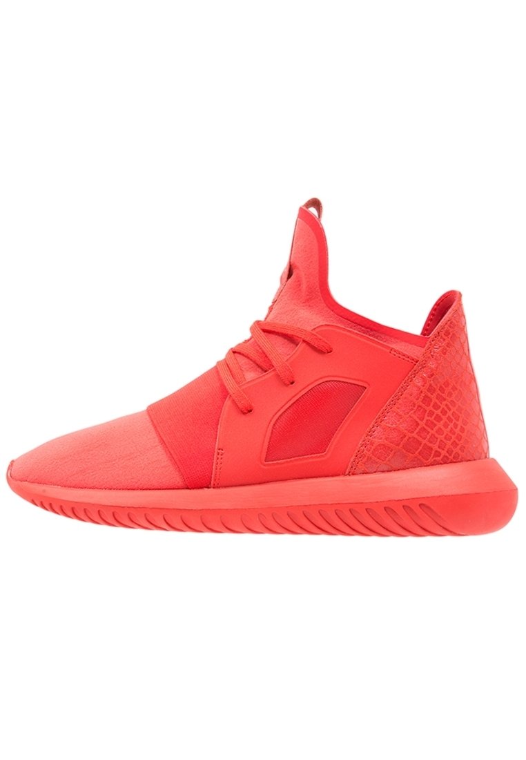 Červené sportovní boty vyrobené z kombinace hladkých a texturovaných materiálů, s elegantním designem, kulatou špičkou a mírně vyvýšenou podrážkou.