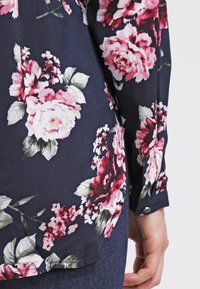 Floral blouse featuring large pink and white roses on a dark navy background, with a button-down cuff and soft fabric texture.
