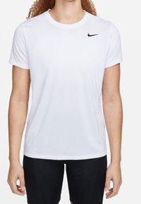 Biała sportowa koszulka Nike z okrągłym dekoltem, krótkimi rękawami oraz czarnym logo Swoosh na lewej piersi. Gładka faktura materiału.