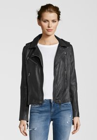 Schwarze Leder-Motorradjacke mit Reißverschlusstaschen, Reverskragen und taillierter Passform, getragen über einem weißen Hemd und blauen Jeans.