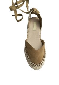 Zapato de esparto de ante marrón con punta en forma de V, suela de yute tejida y lazos de tela beige en el tobillo. Textura suave con detalles de costura decorativa.