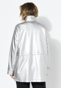 Hopeapintainen satiinitakki, jossa on kaulus, pitkät hihat ja napitettavat hihansuut. Ominaisuuksiin kuuluu rento istuvuus ja sileä, kiiltävä pinta. Takana näkyvä näkymä korostettuna.