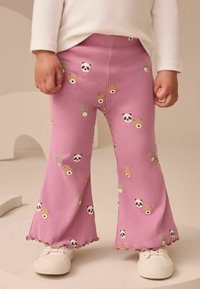 Pantalons roses à côtelés avec un motif ludique de visages d'ours et de pandas, avec un ourlet ondulé, associés à des baskets blanches.