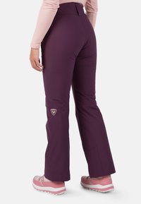 Purple outdoor pants with a fitted waist, flared legs, and logo patch on the thigh, made from a smooth, flexible fabric.