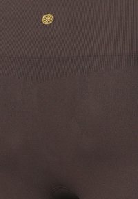 Braune gerippte Leggings mit einer taillierten Passform, die ein kleines goldenes Logo am Bund aufweisen. Das Material wirkt weich und hat eine dezente Textur.