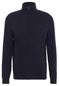 Mörkblå zip-up tröja gjord av ett mjukt stickat material, med hög krage och ribbade ärmslut och nederkant. Minimal logotypdetalj på bröstet.