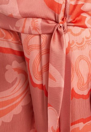 Close-up van roze en oranje patroonstof, in een knoop gebonden, met de nadruk op het gestructureerde materiaal en het abstracte bloemmotief.