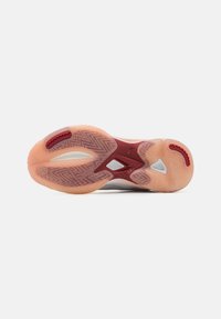 Suola di scarpa sportiva con una base in gomma arancione chiaro traslucida, dettagli rossi e bianchi, modelli testurizzati e un design zigzag distintivo.