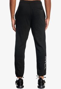 Zwarte sweatpants met een ontspannen pasvorm, voorzien van een achterzak en verticale branding op het linkerpijp. Zacht katoenen materiaal met een gladde textuur.