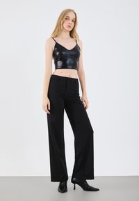 Black leather cropped top with thin straps, paired with high-waisted black wide-leg pants and pointed black heels, set against a neutral background.