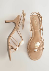 Sandales à talons hauts beiges à fines lanières, ornées de perles décoratives effet marbre, brides à boucle à la cheville, avec le logo "NEXT" sur les semelles intérieures.