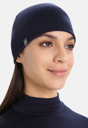 Beanie bleu marine en tissu doux et extensible avec une texture lisse. Doté d'une petite étiquette logo sur le côté. Design ajusté.