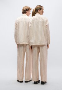 Σετ μπεζ ριγέ τζάκετ και παντελόνι, με μακριά μανίκια, άνετη εφαρμογή και μαύρα παπούτσια. Υφή υφάσματος με διακριτικές κάθετες γραμμές.