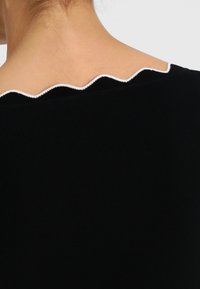 Svart ribbad topp med en vågig vit kant i halslinningen. Fokusera på struktur och kontrast mellan färgerna.