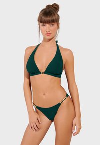 Zielony biustonosz bikini na halter z dekoltem w kształcie litery V, z złotymi akcentami. Pasujące majtki bikini z złotymi ozdobami na biodrach.