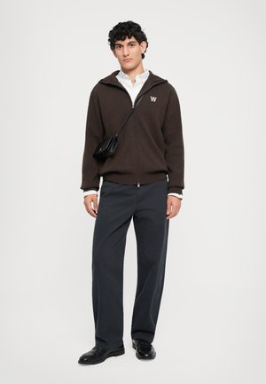 Brown zip-up hoodie with an embroidered logo, paired with dark, wide-leg pants and black shoes; includes a small black crossbody bag.