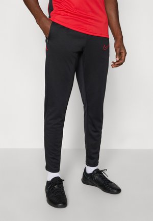 Črne športne hlače s slim fit krojem, ki imajo rdeče poudarke Nike logotipa in stranske žepke. V kombinaciji s črnimi športnimi čevlji in belimi nogavicami.
