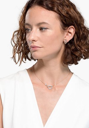 Roséguld hjärtformad halsband med en diamantaccent, med en elegant kedja och en öppen hjärtdesign, bärs med en ljusfärgad topp.