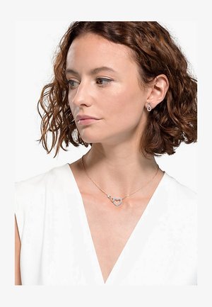 Collana a forma di cuore in oro rosa con un accento di diamante, caratterizzata da una catena delicata e un design del cuore aperto, indossata con una parte superiore di colore chiaro.