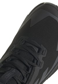 Schwarzer Athletikschuh mit einem strukturierten Obermaterial aus Stoff, verstärkten Überzügen und einer Gummisohle mit einem Profilmuster. Die Schnürsenkel sind integriert für einen sicheren Sitz.