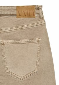 Beżowe jeansy z denimu z widoczną tylną kieszenią, z naszywką ze skóry w kolorze koniakowym z tłoczonym napisem "VMID." Gładka faktura i prosty krój.