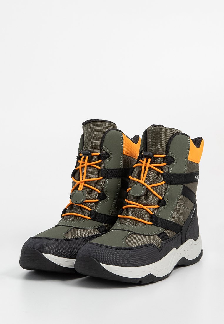 Grüne und schwarze Wanderschuhe mit orangen Schnürsenkeln, gepolsterten Kragen und einem strukturierten Stoffobermaterial. Sie haben eine chunky weiße Sohle und seitliche Akzente.