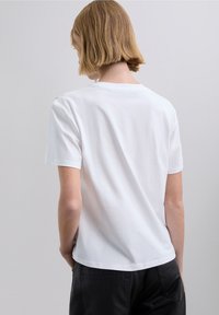 Vit bomulls-t-shirt, korta ärmar, rund halsringning, avslappnad passform. Slät textur utan synliga mönster eller detaljer. Bakifrån.