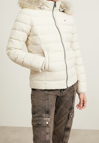 Vaaleanvärinen toppatakki, jossa turkisreunainen huppu, vetoketjukiinnitys, resorit hihansuissa ja vaakasuora tikkauskuvio. Yhdistetty tummiin cargo-housuihin.