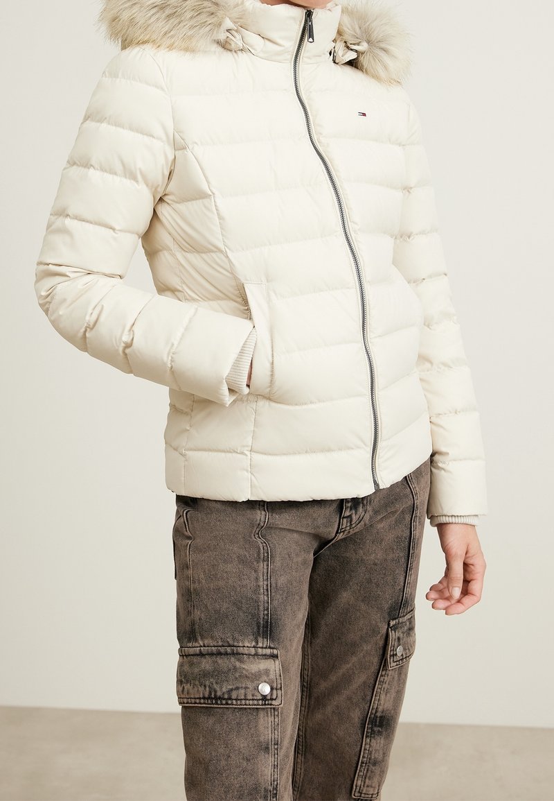 Vaaleanvärinen toppatakki, jossa turkisreunainen huppu, vetoketjukiinnitys, resorit hihansuissa ja vaakasuora tikkauskuvio. Yhdistetty tummiin cargo-housuihin.