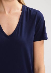 Marinblå V-ringad t-shirt med korta ärmar, tillverkad i mjukt tyg, med en enkel design och slät textur. Inga synliga mönster eller dekorer.