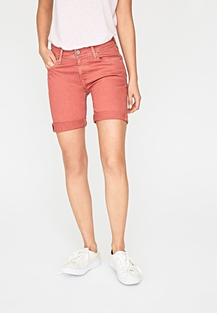 Shorts de mezclilla rojos con dobladillos enrollados, que cuentan con bolsillos frontales y un ajuste regular. Combinados con zapatillas blancas para un look casual.