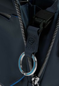 Interior de bolso de cuero azul oscuro con cremallera metálica y clip. Cuenta con un anillo redondo plateado con detalles azules y forro de tela texturizada.