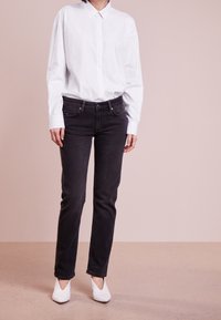 Bílá košile s dlouhými rukávy, spárovaná s černými džíny a bílými lodičkami, na béžovém pozadí.