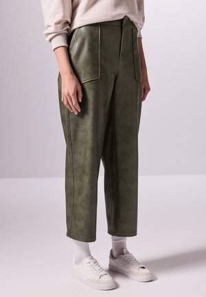 Olijfgroene faux leren broek met twee zakken aan de voorkant, een hoge taille en rechte pijpen, gecombineerd met witte sneakers en enkelsokken.