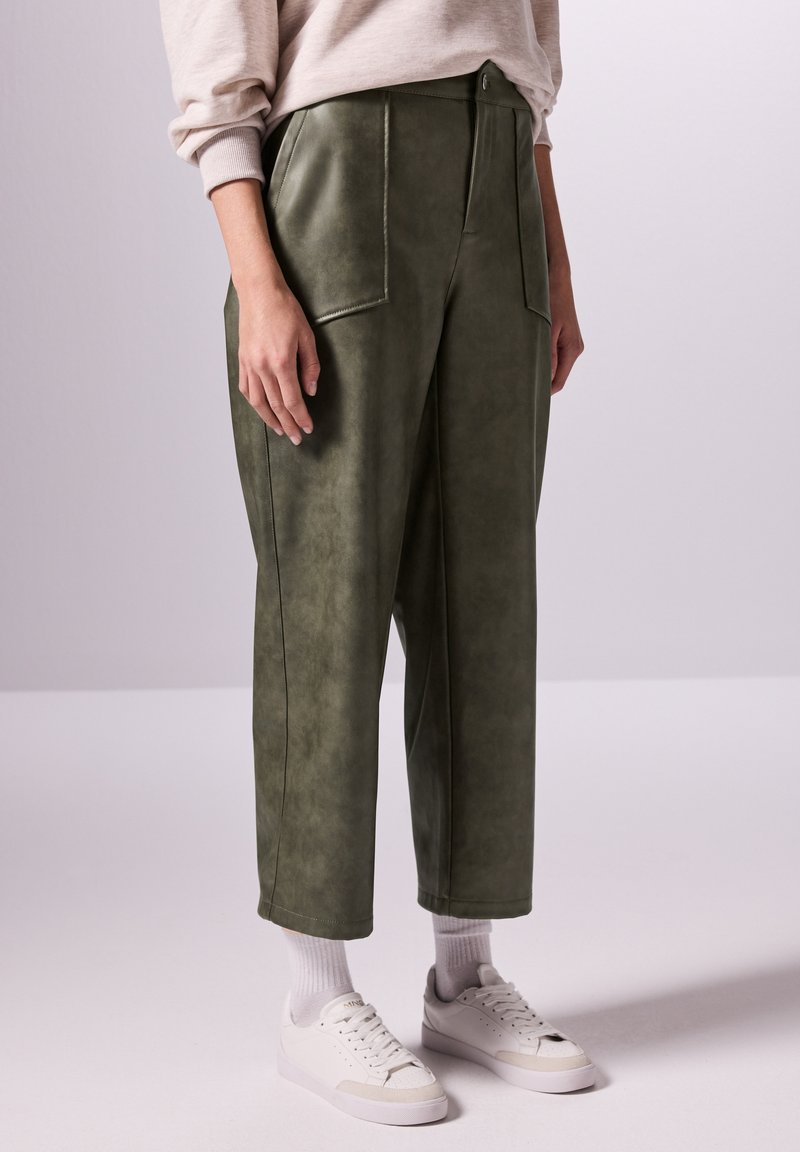 Olivgröna faux läderbyxor med två framfickor, hög midja och raka ben, kombinerat med vita sneakers och ankelsockor.