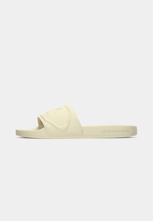 Beige slip-on sandal med prägling och bred rem samt "Calvin Klein Jeans"-logotyp på sidan av sulan.