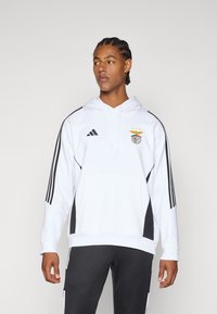 Felpa bianca con cappuccio e pannelli laterali neri, logo Adidas e stemma del Benfica. Presenta una tasca a marsupio e polsini a coste.