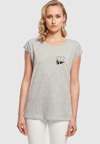 T-shirt en coton gris avec des manches courtes et roulées et un col rond. Présente un petit design brodé d'un cœur et d'une main.