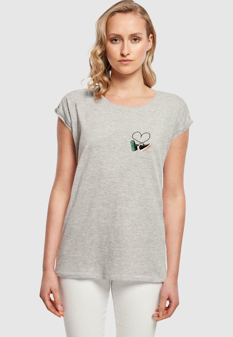 T-shirt en coton gris avec des manches courtes et roulées et un col rond. Présente un petit design brodé d'un cœur et d'une main.