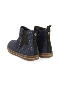 Botas de ante azul marino hasta el tobillo con un corte en forma de estrella, acentos de tachuelas a lo largo de los bordes y una suela de goma texturizada. Paneles laterales elásticos en negro.