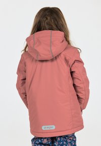 Wasserabweisende, rosa Jacke mit Kapuze und blauen Akzenten; hat ein Logo-Patch auf der Rückseite. Getragen über Blumenmuster-Hosen.