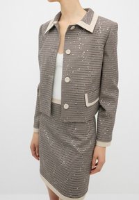 Ensemble blazer et jupe en damier marron et crème, avec des accents de sequins, col cranté et fermeture à bouton sur le blazer.