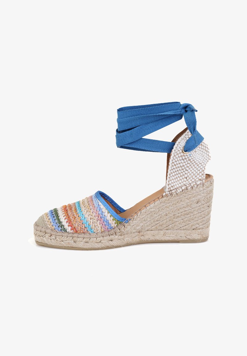 Sandale compensée avec un dessus en tissu rayé multicolore tressé, des brides de cheville bleues, un talon compensé en jute et une semelle intérieure en cuir.