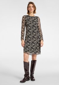 Langärmliges Kleid mit einem abstrakten Muster in Schwarz und Beige, versehen mit einem runden Halsausschnitt und transparenten Ärmeln, kombiniert mit glänzenden burgunderroten kniehohen Stiefeln.