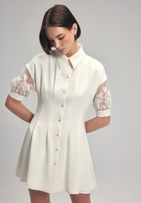 Witte jurk met een gepersonaliseerd ontwerp, korte mouwen met sheer stof en ingewikkelde kant borduursels, knoopsluiting aan de voorkant en een uitlopende rok.