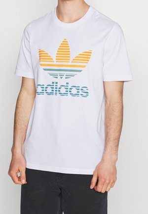 Biała bawełniana koszulka z krótkim rękawem z wielokolorowym, paskowanym wzorem logo Adidas w odcieniach żółtego, pomarańczowego i niebieskiego na klatce piersiowej.