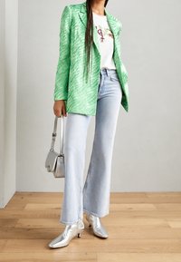 Blazer a rayas verdes, camiseta gráfica blanca, pantalones vaqueros acampanados de un azul claro, botas de tobillo plateadas y un pequeño bolso de mano plateado.