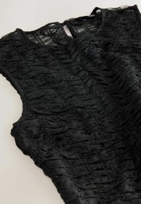 Black sleeveless top with textured, crinkled fabric. Features a rounded neckline and visible seam detailing throughout the design.